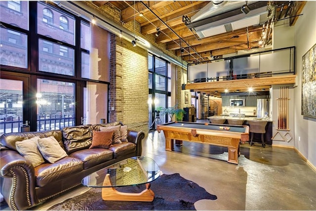 rec room with brick wall, a towering ceiling, billiards, beam ceiling, and concrete flooring