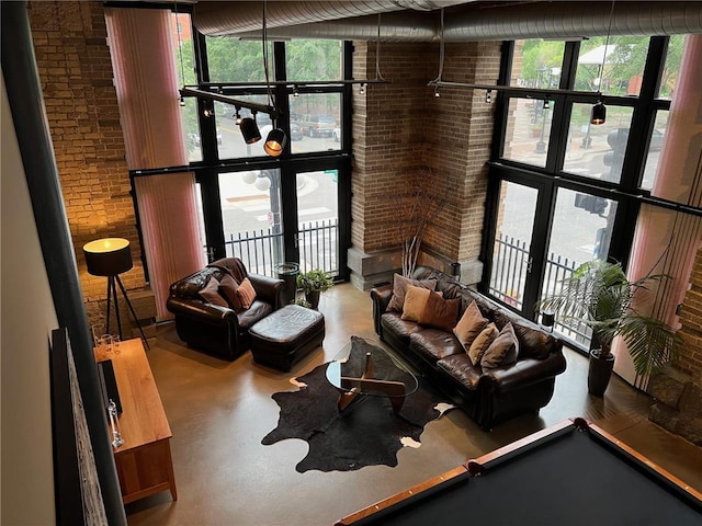 living room featuring a high ceiling, a healthy amount of sunlight, brick wall, and pool table