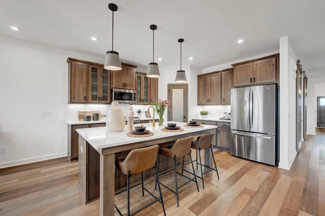 kitchen with hanging light fixtures, stainless steel appliances, light hardwood / wood-style flooring, an island with sink, and a kitchen bar