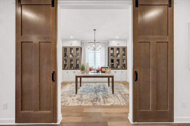 interior space with a barn door, light wood-type flooring, and an inviting chandelier