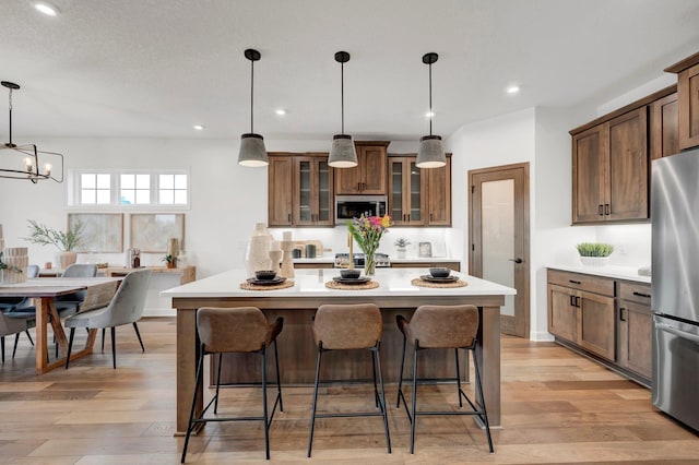 kitchen with light wood-type flooring, stainless steel appliances, a notable chandelier, a center island, and hanging light fixtures