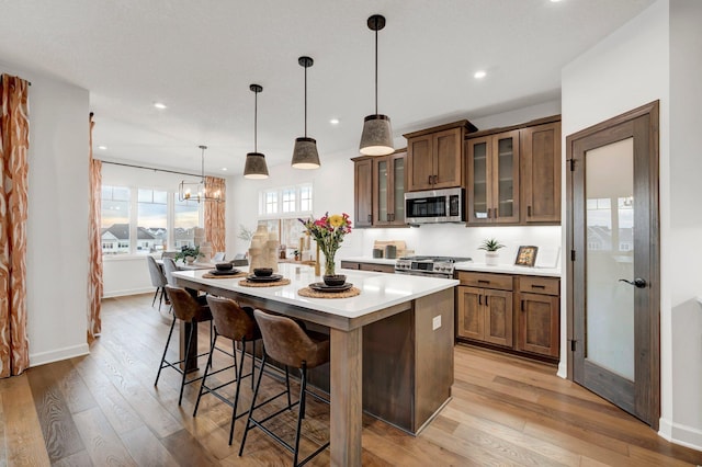 kitchen with a breakfast bar, hanging light fixtures, light hardwood / wood-style floors, appliances with stainless steel finishes, and a kitchen island