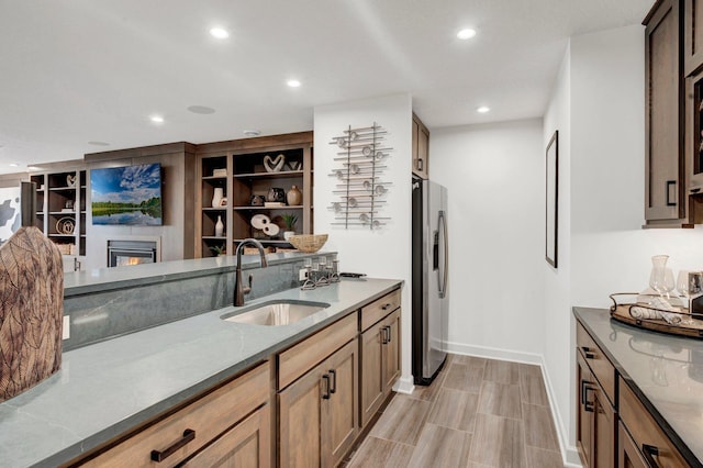 kitchen featuring built in shelves, stainless steel fridge, sink, and light stone counters