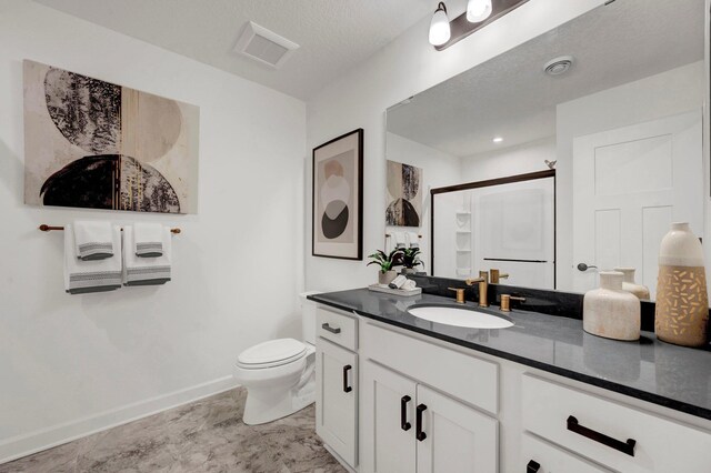 bathroom with vanity, toilet, a shower with shower door, and a textured ceiling