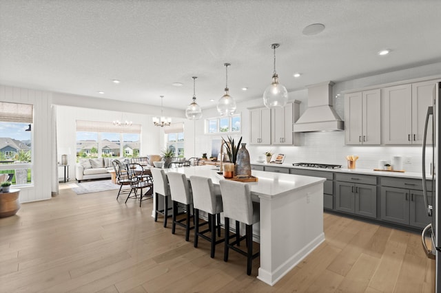 kitchen with a breakfast bar, stainless steel gas stovetop, hanging light fixtures, a kitchen island with sink, and custom range hood