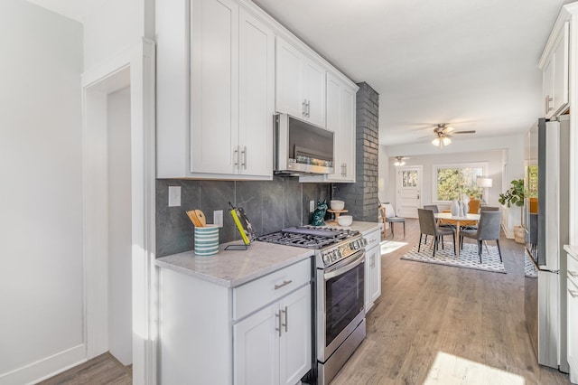 kitchen with white cabinets, ceiling fan, light wood-type flooring, appliances with stainless steel finishes, and tasteful backsplash