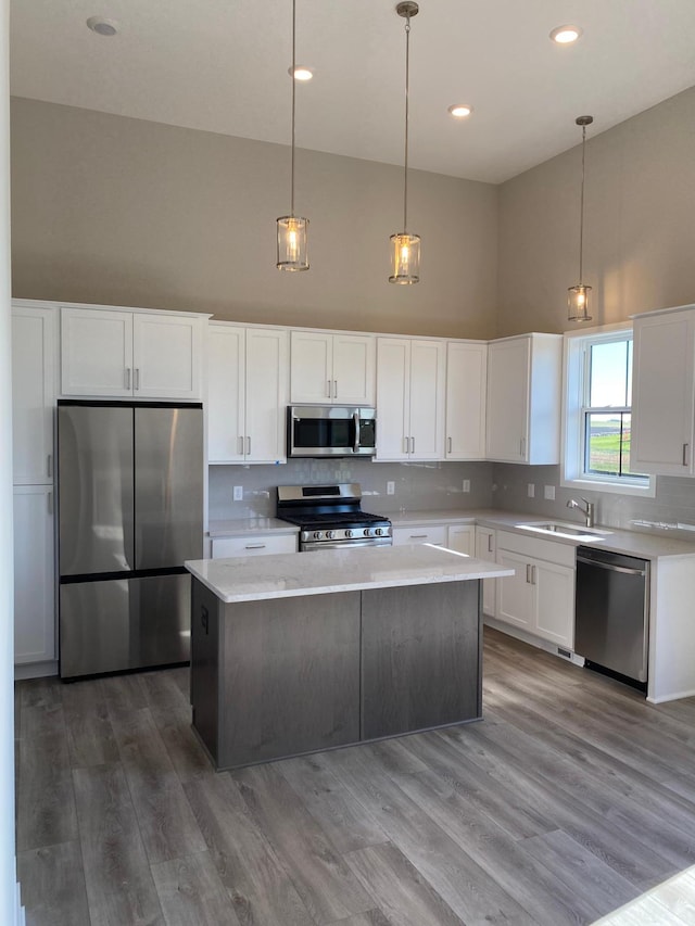 kitchen featuring pendant lighting, white cabinets, hardwood / wood-style flooring, a high ceiling, and stainless steel appliances