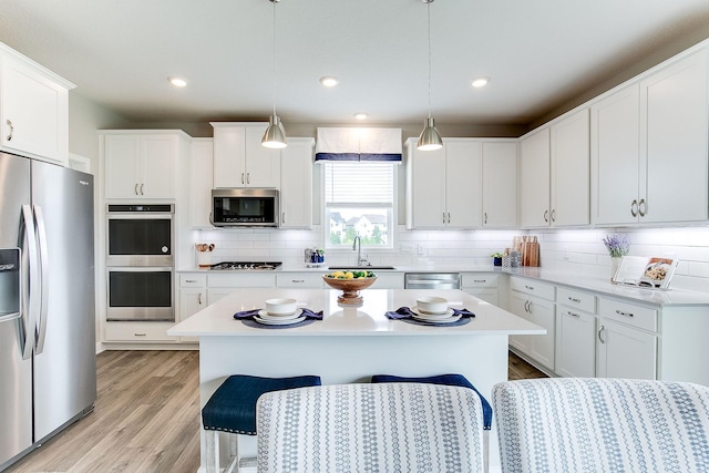 kitchen with stainless steel appliances, white cabinetry, hanging light fixtures, and a kitchen island