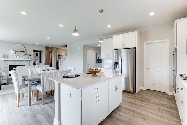 kitchen featuring stainless steel fridge, a kitchen island, a fireplace, white cabinetry, and hanging light fixtures