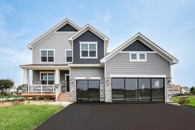 craftsman house with a garage, driveway, a porch, and stone siding