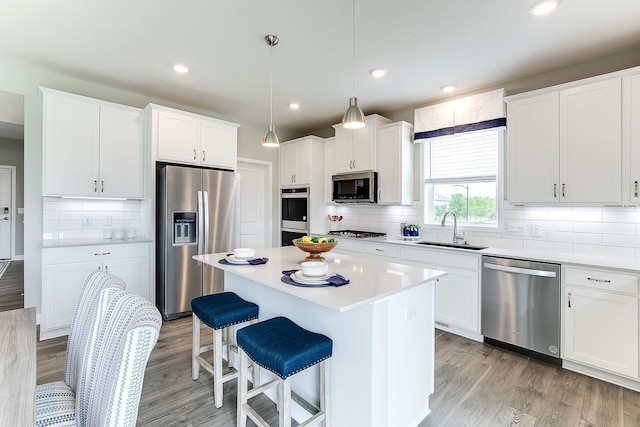 kitchen featuring stainless steel appliances, a sink, light wood-style floors, a kitchen island, and a kitchen bar