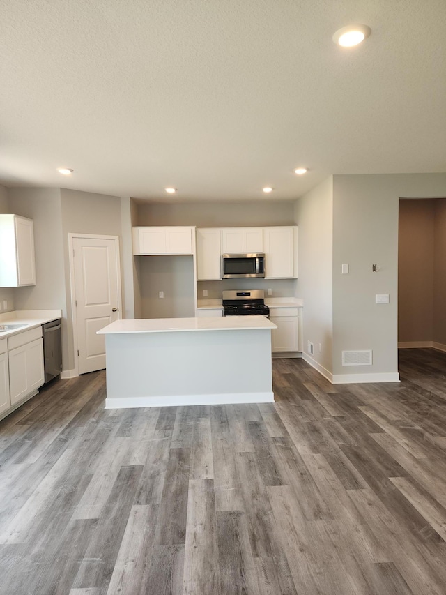 kitchen with appliances with stainless steel finishes, light wood-type flooring, sink, a center island, and white cabinetry