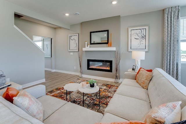 living area featuring baseboards, recessed lighting, wood finished floors, and a glass covered fireplace