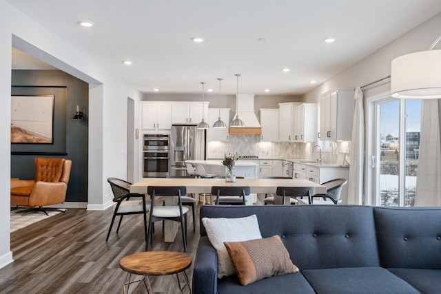 kitchen featuring custom exhaust hood, appliances with stainless steel finishes, hanging light fixtures, white cabinets, and tasteful backsplash