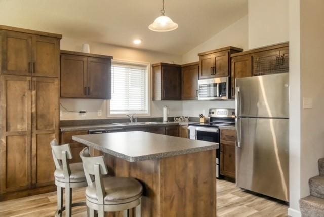 kitchen with a center island, hanging light fixtures, vaulted ceiling, light hardwood / wood-style flooring, and appliances with stainless steel finishes