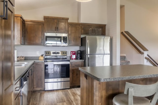 kitchen with a kitchen breakfast bar, stainless steel appliances, vaulted ceiling, sink, and light hardwood / wood-style floors