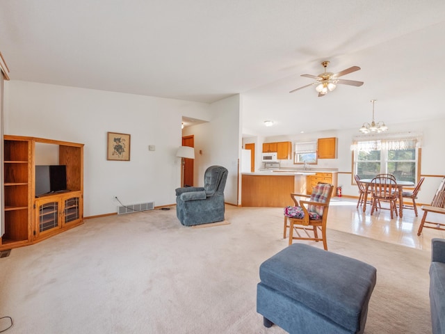 carpeted living room with ceiling fan with notable chandelier and vaulted ceiling