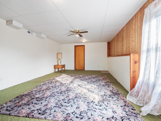 spare room with ceiling fan, a drop ceiling, and wood walls