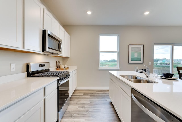 kitchen with appliances with stainless steel finishes, light wood-type flooring, white cabinetry, and sink