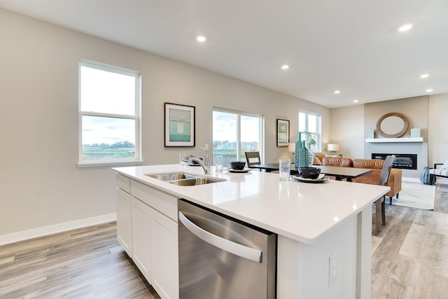 kitchen with white cabinets, sink, dishwasher, light hardwood / wood-style floors, and an island with sink