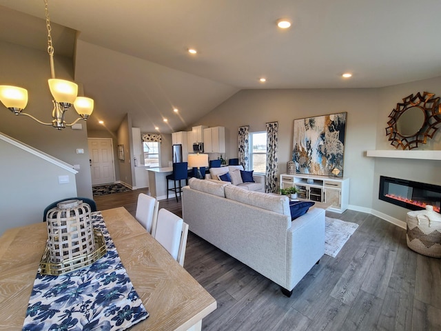 living room featuring plenty of natural light, dark wood-type flooring, lofted ceiling, and an inviting chandelier