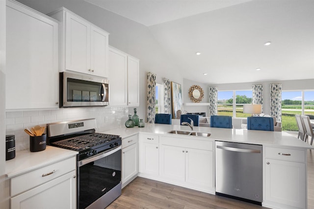 kitchen with sink, stainless steel appliances, kitchen peninsula, lofted ceiling, and decorative backsplash