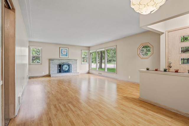 unfurnished living room with an inviting chandelier, light wood-type flooring, and a brick fireplace