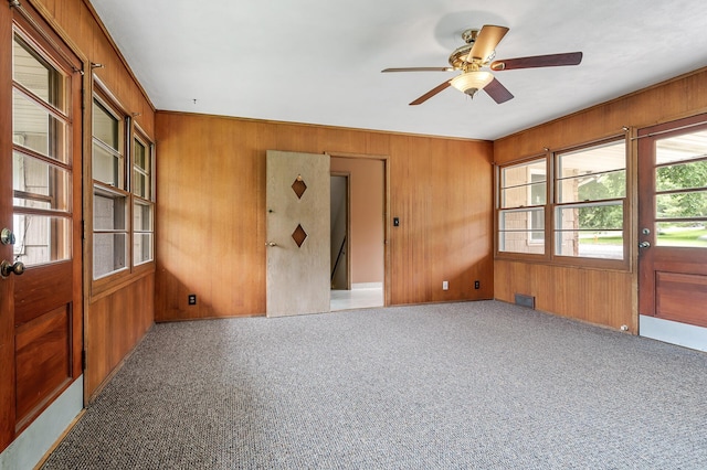 carpeted spare room featuring ceiling fan and wood walls