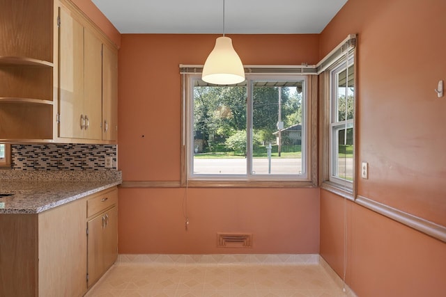 kitchen with light stone countertops, backsplash, decorative light fixtures, and a healthy amount of sunlight