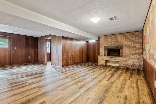 unfurnished living room with a textured ceiling, light wood-type flooring, a fireplace, and wooden walls