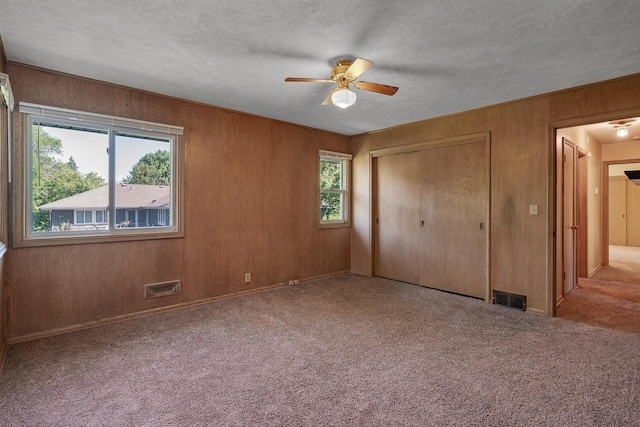 unfurnished bedroom with ceiling fan, a textured ceiling, wooden walls, and light carpet