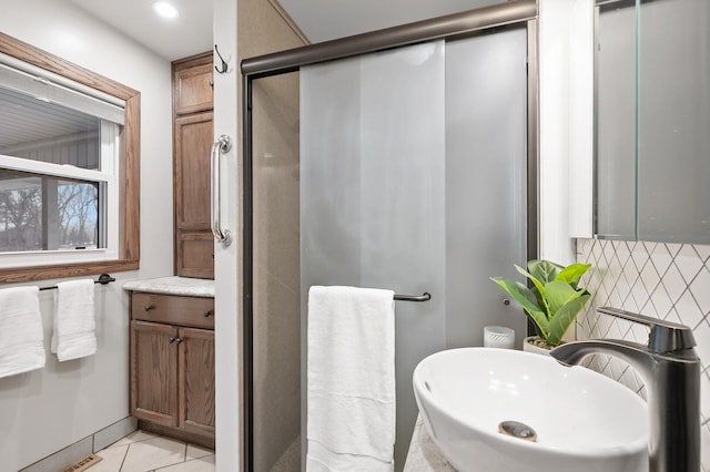 bathroom with tile patterned flooring, decorative backsplash, a shower with door, and sink