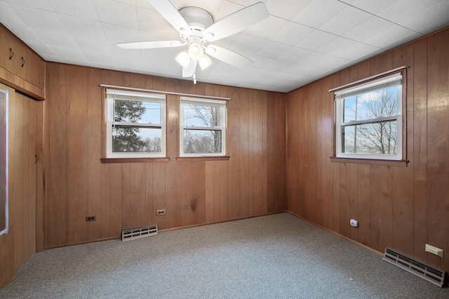 unfurnished room with carpet flooring, ceiling fan, and wood walls