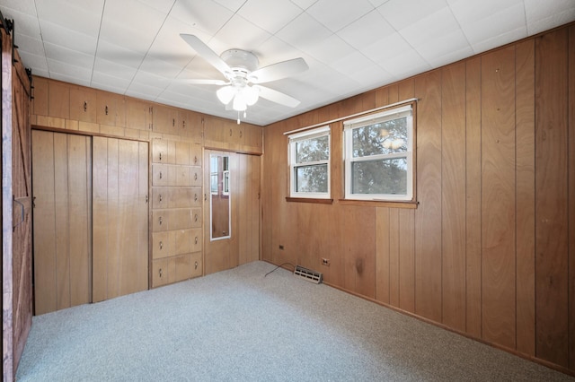 spare room with carpet floors, a barn door, ceiling fan, and wooden walls