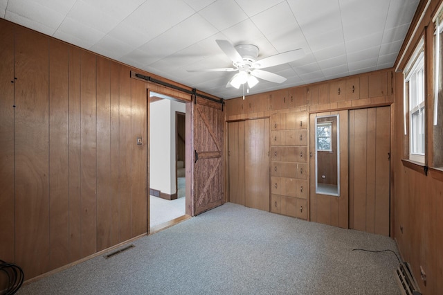 unfurnished bedroom featuring a barn door, light colored carpet, ceiling fan, and wooden walls