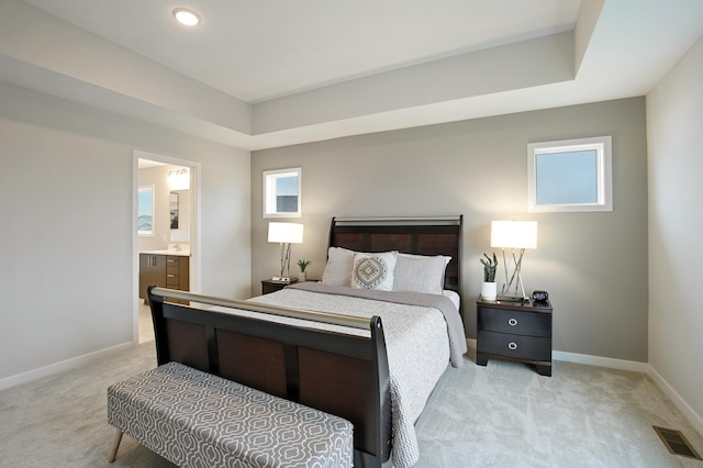 carpeted bedroom with ensuite bathroom and a tray ceiling