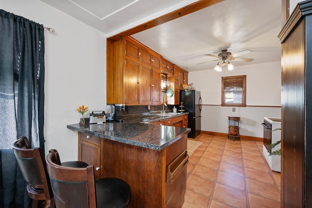 kitchen featuring kitchen peninsula, black fridge, ceiling fan, white electric range, and light tile patterned flooring