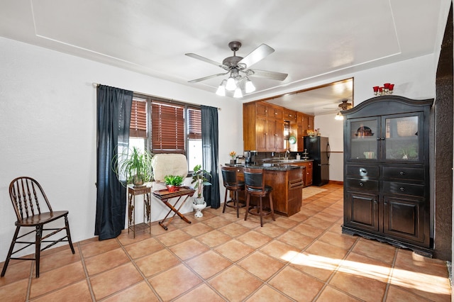 kitchen featuring ceiling fan, black fridge, kitchen peninsula, a breakfast bar area, and light tile patterned floors