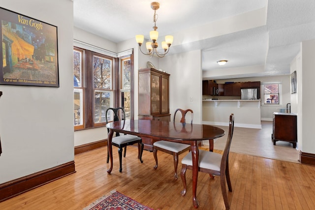 dining room with light wood-type flooring, an inviting chandelier, and a tray ceiling