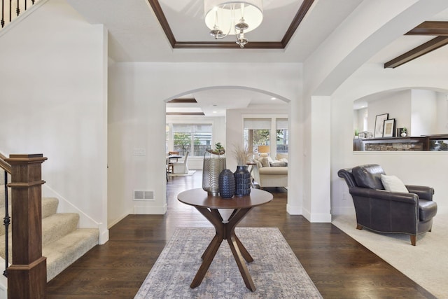 entrance foyer featuring dark hardwood / wood-style flooring, a tray ceiling, ornamental molding, and a chandelier