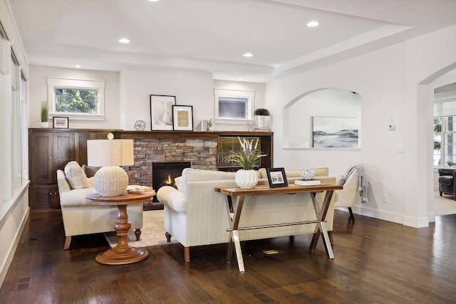 interior space with a stone fireplace, dark hardwood / wood-style floors, and a tray ceiling