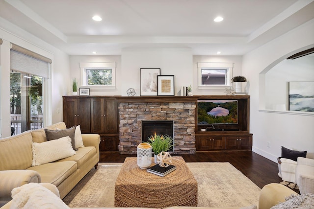 living room featuring a stone fireplace, dark hardwood / wood-style floors, and a tray ceiling