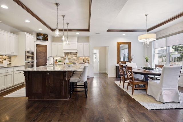 kitchen featuring hanging light fixtures, a tray ceiling, and an island with sink