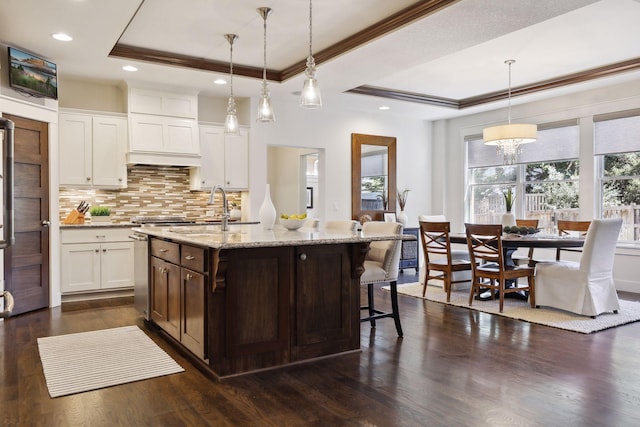 kitchen featuring pendant lighting, sink, white cabinets, a center island with sink, and a raised ceiling