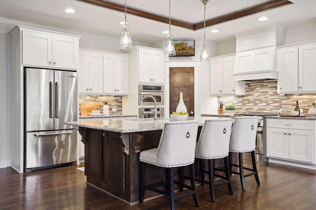 kitchen with appliances with stainless steel finishes, pendant lighting, white cabinets, a kitchen bar, and a kitchen island with sink