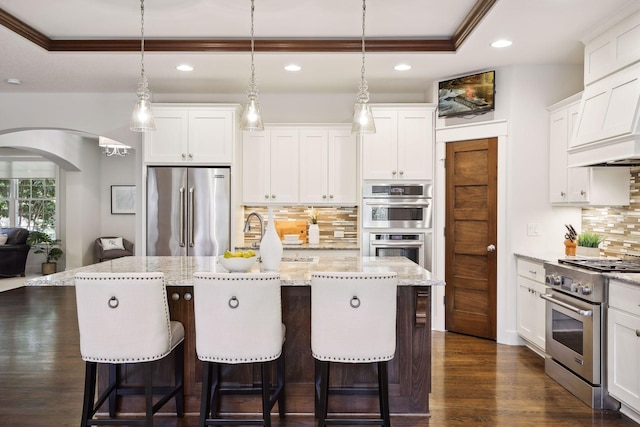 kitchen with high end appliances, pendant lighting, white cabinets, and a center island with sink