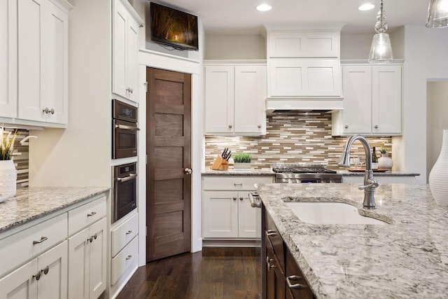 kitchen with sink, white cabinets, light stone counters, and decorative light fixtures