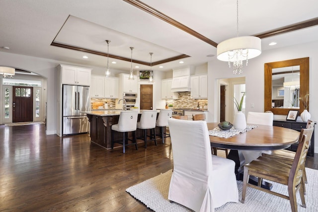 dining space featuring dark wood-type flooring, sink, an inviting chandelier, crown molding, and a tray ceiling