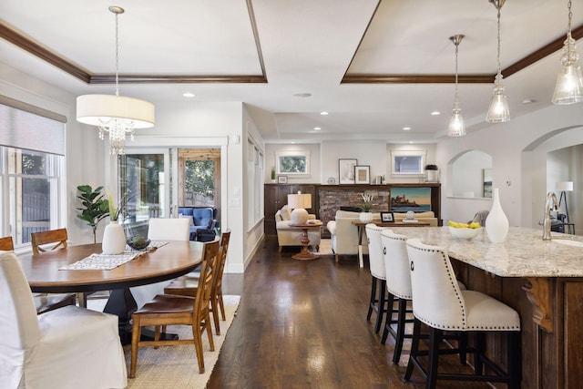 dining area featuring sink, crown molding, dark hardwood / wood-style flooring, a raised ceiling, and a fireplace