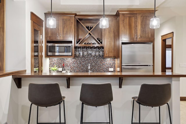 kitchen featuring hanging light fixtures, appliances with stainless steel finishes, backsplash, and a kitchen breakfast bar